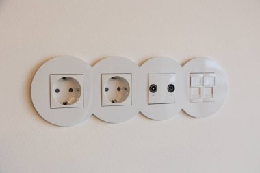 Elektrik prizleri, televizyon ve internet portları ve minimalist iç mekânlarda ışık anahtarları olan modern beyaz duvar..