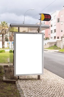 Sakin bir şehir caddesi boyunca bir otobüs durağı barınağında boş bir reklam panosu modeli. Boş reklam paneli, arka planda konut binaları ve trafik ışıkları bulunan markalaşma ve pazarlama kampanyaları için temiz bir kopya alanı sunuyor..