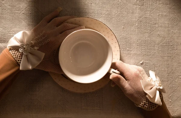 Hands of the girl wearing the vintage gloves with decore and holding a vintage cup