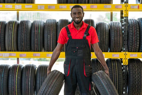 Smiling mechanic with a tire over garage tires shop background