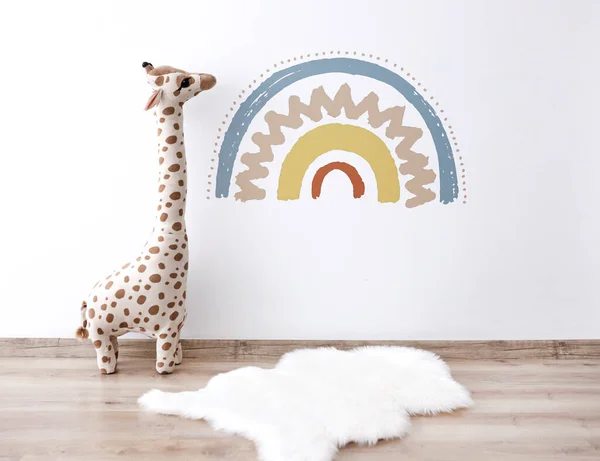 Gökkuşağı desenini beyaz duvara yapıştırıyorum. Oyuncak zürafa bebek odası. İskandinav tasarımı.