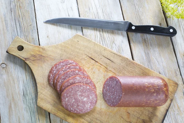 Salami rebanado junto a un cuchillo en una tabla de cortar marrón — Foto de Stock