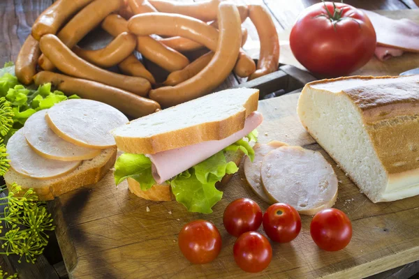 Embutidos, tomates y sándwich en la mesa de madera — Foto de Stock