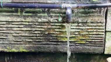 Eski bir metal borudan su sızıyor. Boru yıpranmış taş bir duvara monte edilmiş. Su sürekli akar, atıkların görüntüsünü oluşturur..