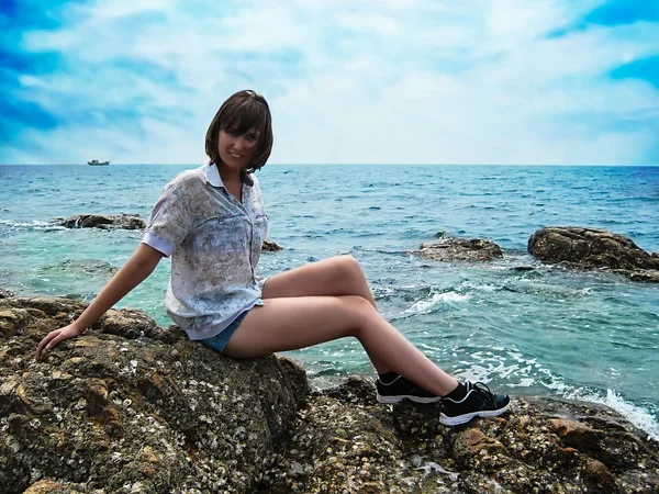 Pěkná usměvavá dívka sedí na kameni na mořském pozadí — Stock fotografie