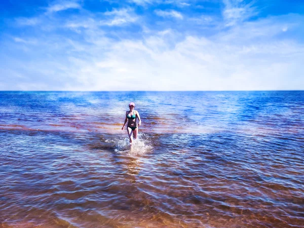 Hermosa joven mujer caminando entre el agua brillante del mar azul — Foto de Stock