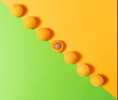 Taze kayısı meyvesi çapraz olarak pastel yeşil ve sarı-turuncu düz kompozisyona karşı dizilmiştir. Orta kayısı görünür kayısı taşıyla ikiye bölünmüş..