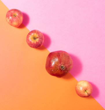 Üç taze organik elma meyvesi ve pastel pembe ve turuncu düz kompozisyona karşı köşegen çizilmiş bir nar..