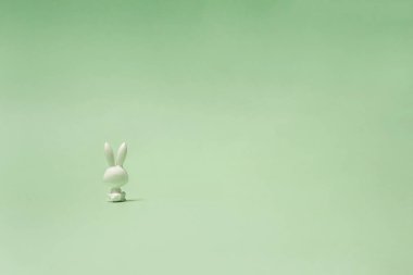 Yalnız bir oyuncak tavşan oturmuş ve pastel yeşil bir mesafede dik dik bakıyor. Tavşanın sırtı..
