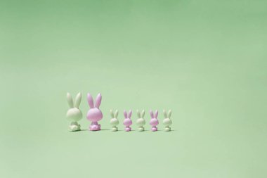 Beyaz ve pembe renkli yedi oyuncak tavşan pastel yeşil bir mesafede oturuyor ve onlara bakıyor. Tavşanların sırtı fotoğrafı..