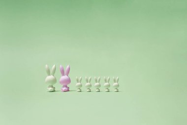 Beyaz ve pembe renkli yedi oyuncak tavşan pastel yeşil bir mesafede oturuyor ve onlara bakıyor. Tavşanların sırtı fotoğrafı..