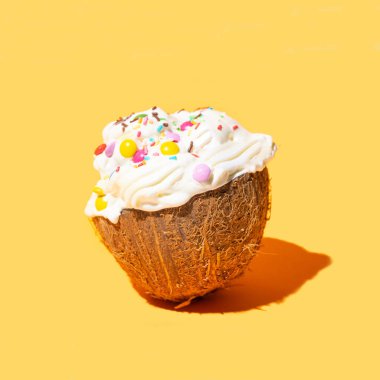 Taze çiğ organik hindistan cevizinin yarısı beyaz tatlı kremayla dolu ve üzeri renkli süslemelerle dolu. Sıcak turuncu arkaplan.