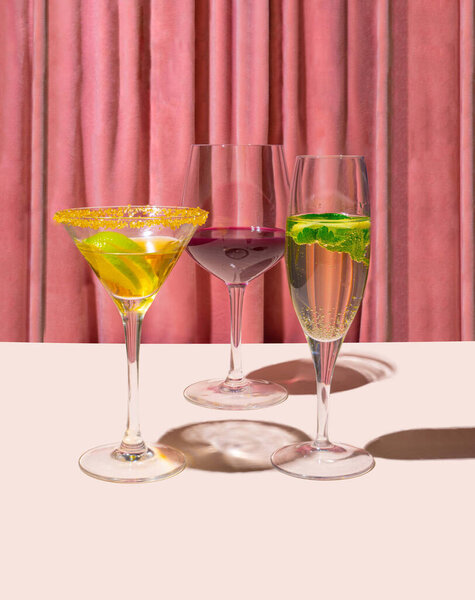 Three glasses with cocktail, champagne and vine in front of reach pink renaissance velvet curtain. Retro theatre vibe.