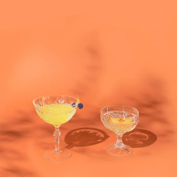 一つのガラスの上に二つのチョークベリーがある オレンジを背景に魔法のカクテルと2つの印象的なクリスタルグラス ムーディは周りの雰囲気を冷ます — ストック写真