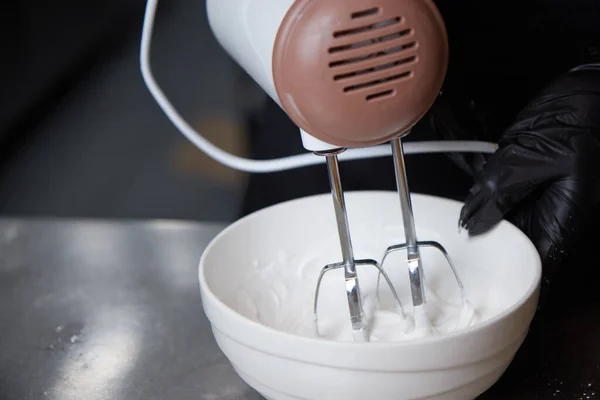cook with gloved hands whips the dough in a plate with a white mixer