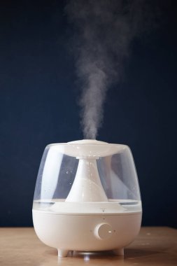 Masadaki beyaz buhar jeneratörü ayakta duruyor. Yan taraftan buhar görüntüsü yayıyor.