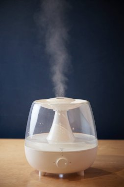Masadaki beyaz buhar jeneratörü ayakta duruyor. Yan taraftan buhar görüntüsü yayıyor.