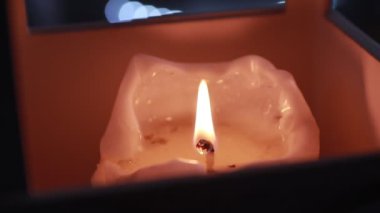 Mum alevi, çerçevenin ortasındaki mum tutacağının içinde yanıyor. Arka plan odak dışı.