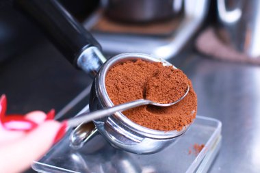 Yakın plan, mutfak terazisinde kahve tutacağı filtrede kahve çekirdekleri kaşıkta kahve, arka plan bulanık.