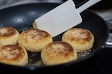 Peynirli kekler tavada kızartılır. Aşçı hamuru kaşıkla çevirir. Arka plan bulanıklaşır.