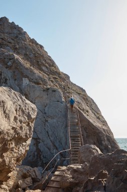 a man climbs a stone staircase in the rock, sea and mountains, rocks, extreme