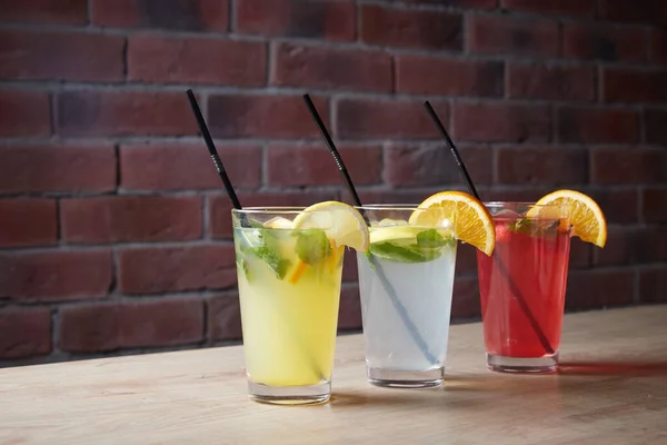На столе, безалкогольные напитки, различные коктейли, стакан с соломинкой и ломтиком лимона, размытый фон — стоковое фото