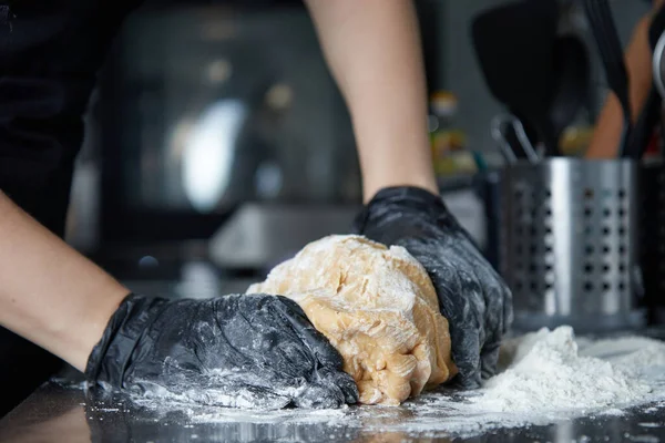 Cocinar con las manos guantes amasa la masa en la vista lateral de la mesa — Foto de Stock