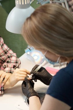 Tırnak servisinin ustası manikür yapıyor, cilayla kaplıyor ve tırnaklarını büyütüyor.