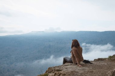 girl sitting on a rock, view from the back, autumn landscape, mountains and fog
