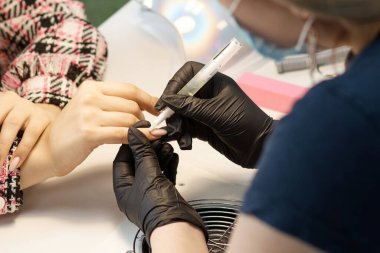 Tırnak servisinin ustası manikür yapıyor, cilayla kaplıyor ve tırnaklarını büyütüyor.