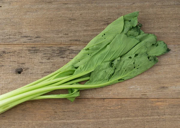 Withered mustard green on shabby wooden board.