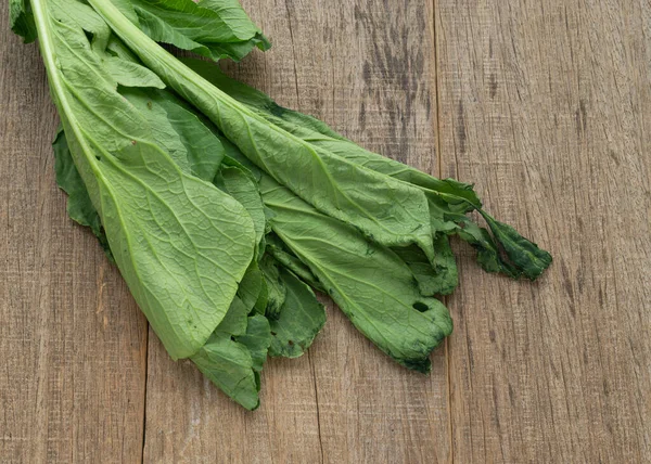 Withered mustard green on shabby wooden board.