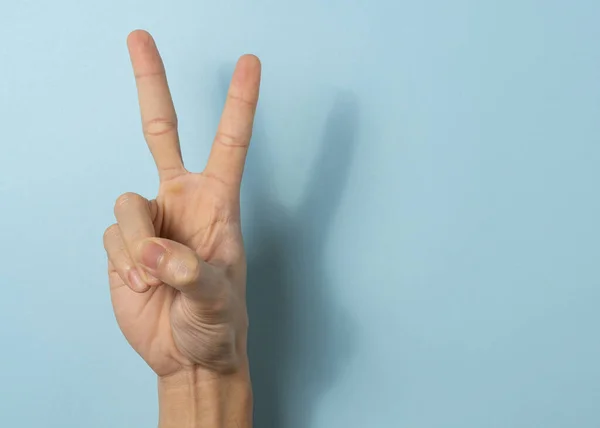 Hand a man show peace sign on blue background with a copy space.