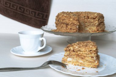 Bir dilim Napolyon keki ve arka planda beyaz bir fincan çay.