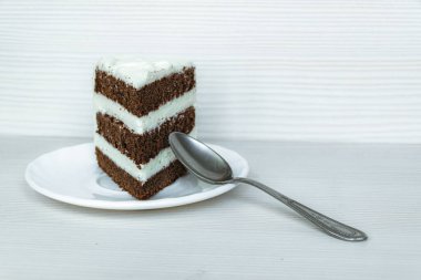 Solda tatlı kaşığı ve tereyağı kremalı bir parça çikolatalı kek yer almaktadır. Beyaz arkaplan