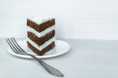 Solda bir çatal ve bir parça tereyağlı çikolatalı pandispanya var. Beyaz arkaplan