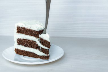 Bir çatal, solunda krema bulunan çikolatalı keki deliyor..