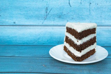 Sağında tereyağı kremi olan bir dilim çikolatalı kek. Mavi arka plan. Yakın plan..