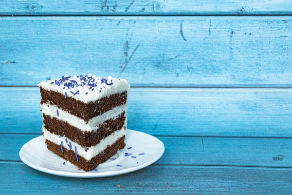 左側にバタークリームの層があるチョコレートスポンジケーキ 紫のスプリンクル 青の背景 — ストック写真