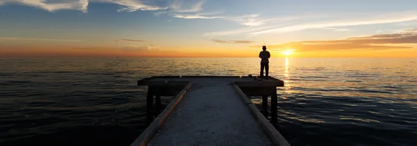 Homem solitário pesca sozinho durante o pôr do sol Imagens Royalty-Free