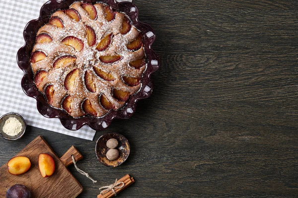 Pflaumenkuchen und Zutaten auf dunklem Holztisch — Stockfoto