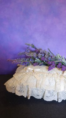 Mor arka planda beyaz dantel bir yastığın üzerinde bir demet lavanta çiçeği.