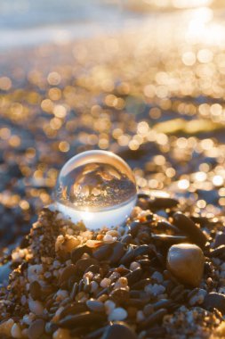 Plajdaki cam yuvarlak top yazın gün batımında denizi yansıtır.