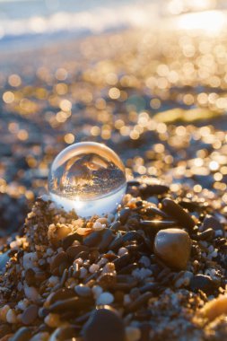 Plajdaki cam yuvarlak top yazın gün batımında denizi yansıtır.