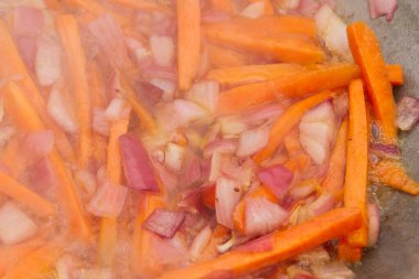 Kırmızı soğanlı havuç dilimleri ızgaradaki bir kazanda kızartılır.