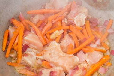 Tavuk parçaları ızgarada havuç ve kırmızı soğanla kızartılır.