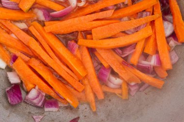 Kırmızı soğanlı havuç dilimleri ızgaradaki bir kazanda kızartılır.