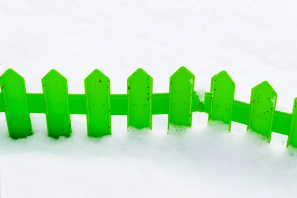 Green plastic fence in the snow in the garden in winter