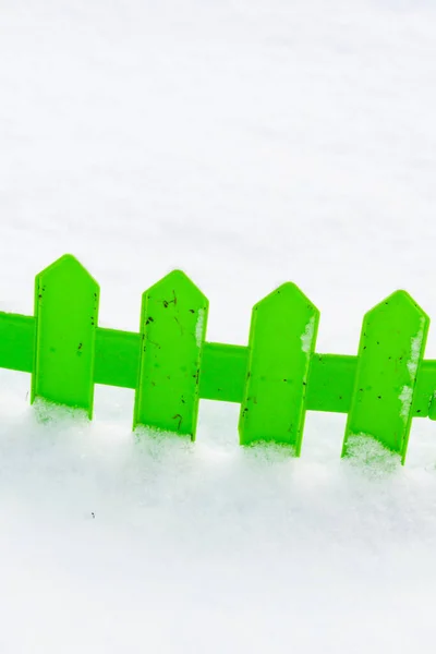 Green plastic fence in the snow in the garden in winter