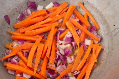 Kırmızı soğanlı havuç dilimleri ızgaradaki bir kazanda kızartılır.